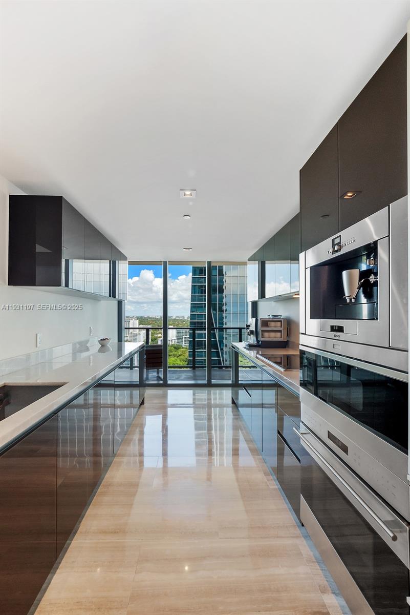 A modern galley kitchen features dark glossy cabinetry, stainless steel appliances, and a balcony view — 1451 Brickell Ave # 2405, Miami FL 33131, MIAMI, FL