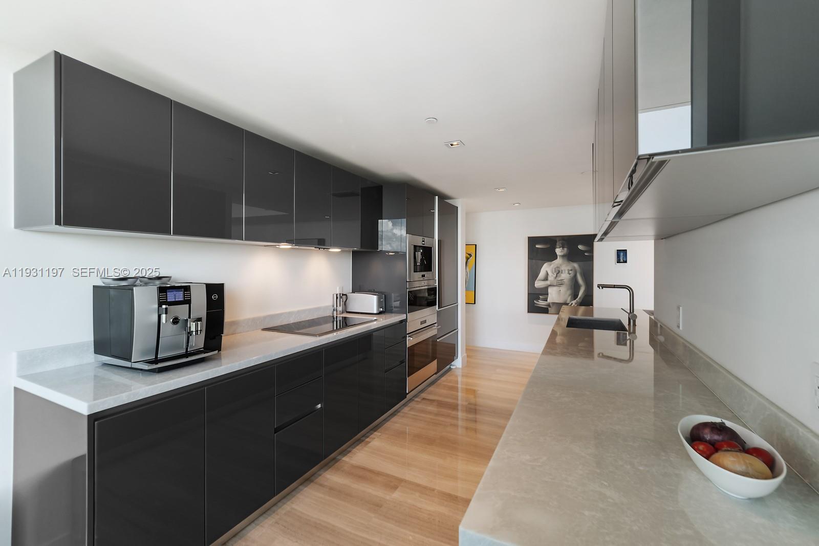 A modern galley kitchen features dark glossy cabinetry, light stone countertops, and light wood flooring — 1451 Brickell Ave # 2405, Miami FL 33131, MIAMI, FL