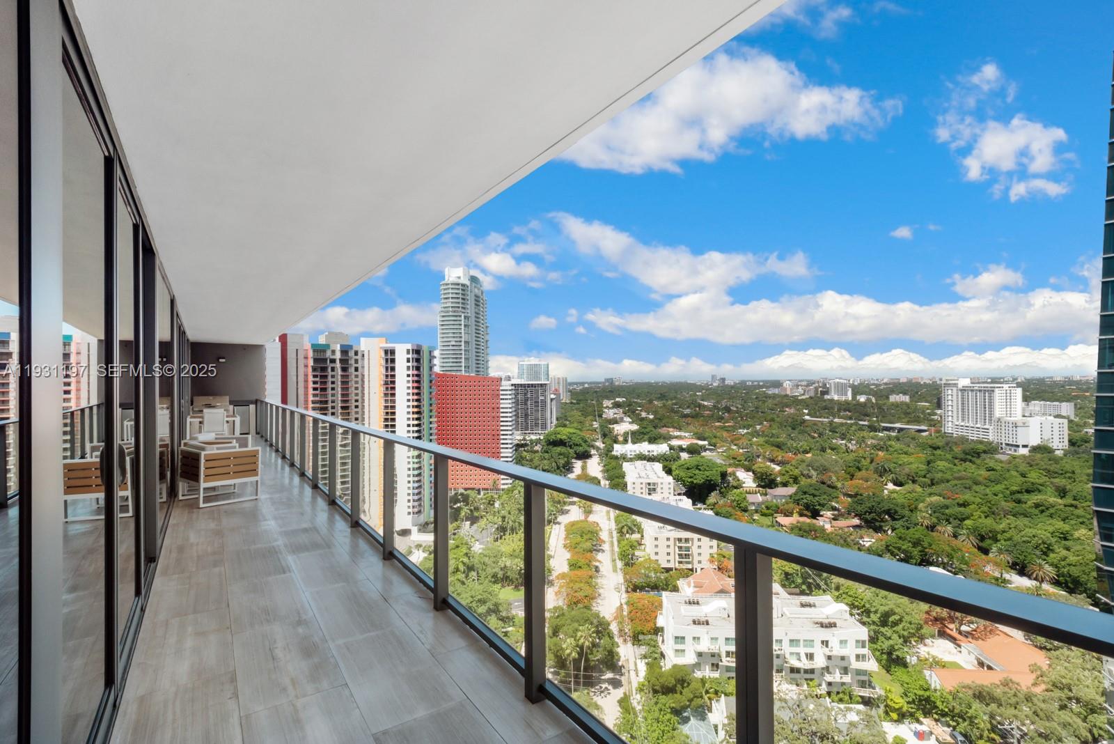 A balcony with tile flooring overlooks a city skyline and a dense green landscape — 1451 Brickell Ave # 2405, Miami FL 33131, MIAMI, FL