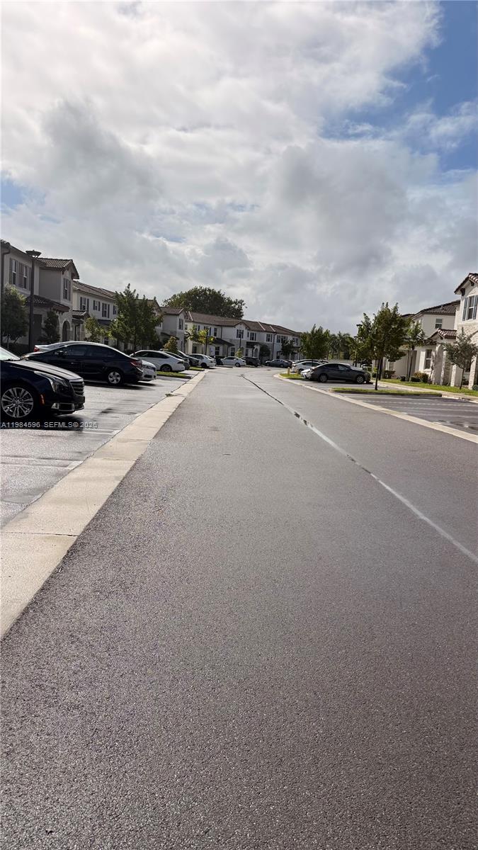 A paved street runs between rows of residential townhouses with parked cars on both sides — 12383 NW 23rd Ct, Miami FL 33167, MIAMI, FL