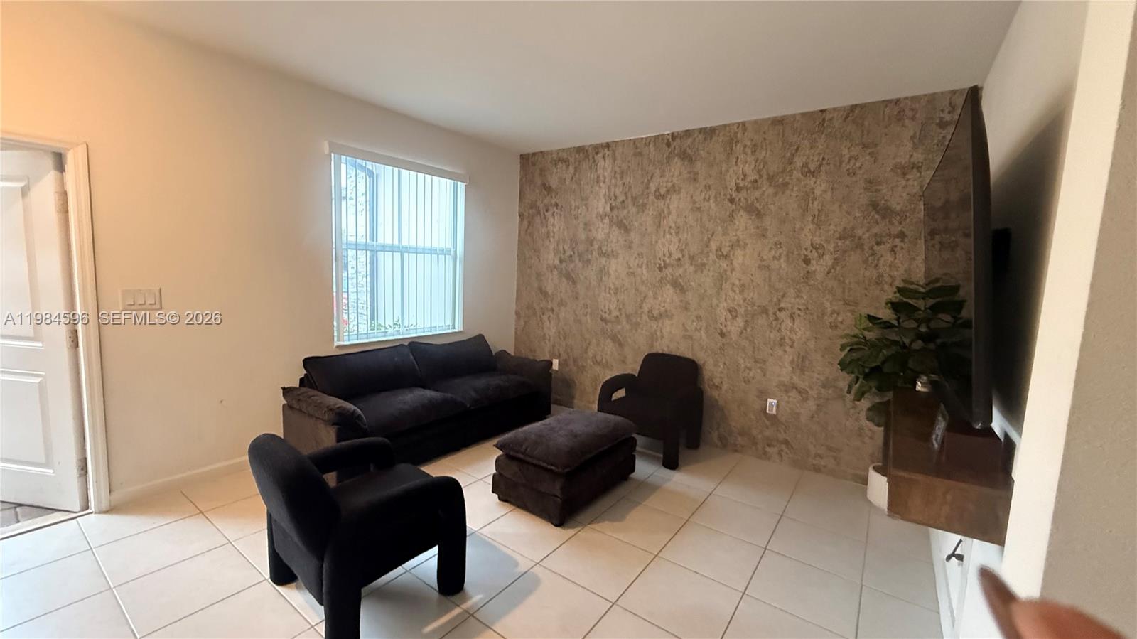 A living room features a textured accent wall, tile flooring, and dark upholstered furniture — 12383 NW 23rd Ct, Miami FL 33167, MIAMI, FL