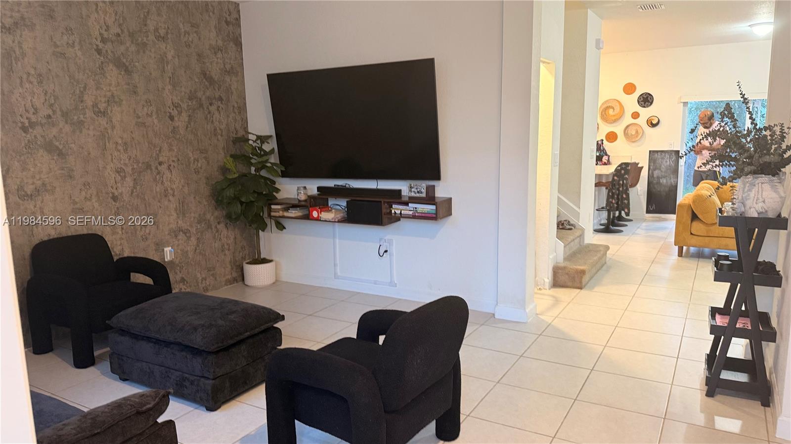 A living room features a textured accent wall, a wall-mounted television, and black furniture — 12383 NW 23rd Ct, Miami FL 33167, MIAMI, FL