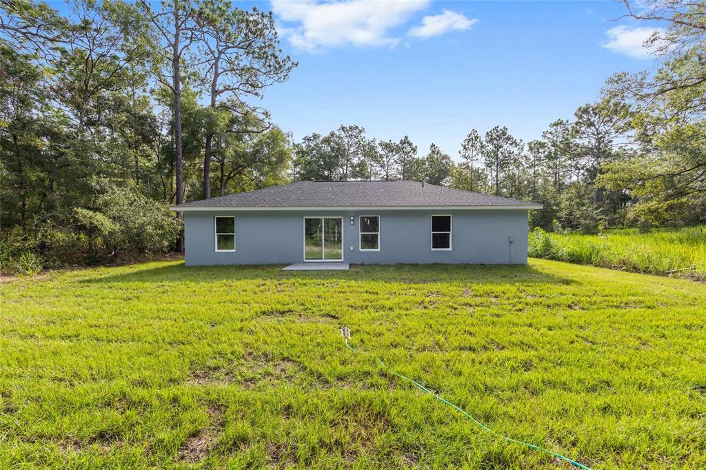The rear exterior of a single-story gray house with a sliding glass door and windows — 2110 SW 159TH COURT, OCALA, FL