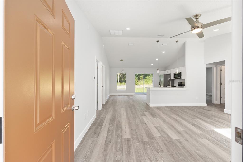 An open-concept living area with light wood-look flooring and a kitchen viewed from a doorway — 2110 SW 159TH COURT, OCALA, FL