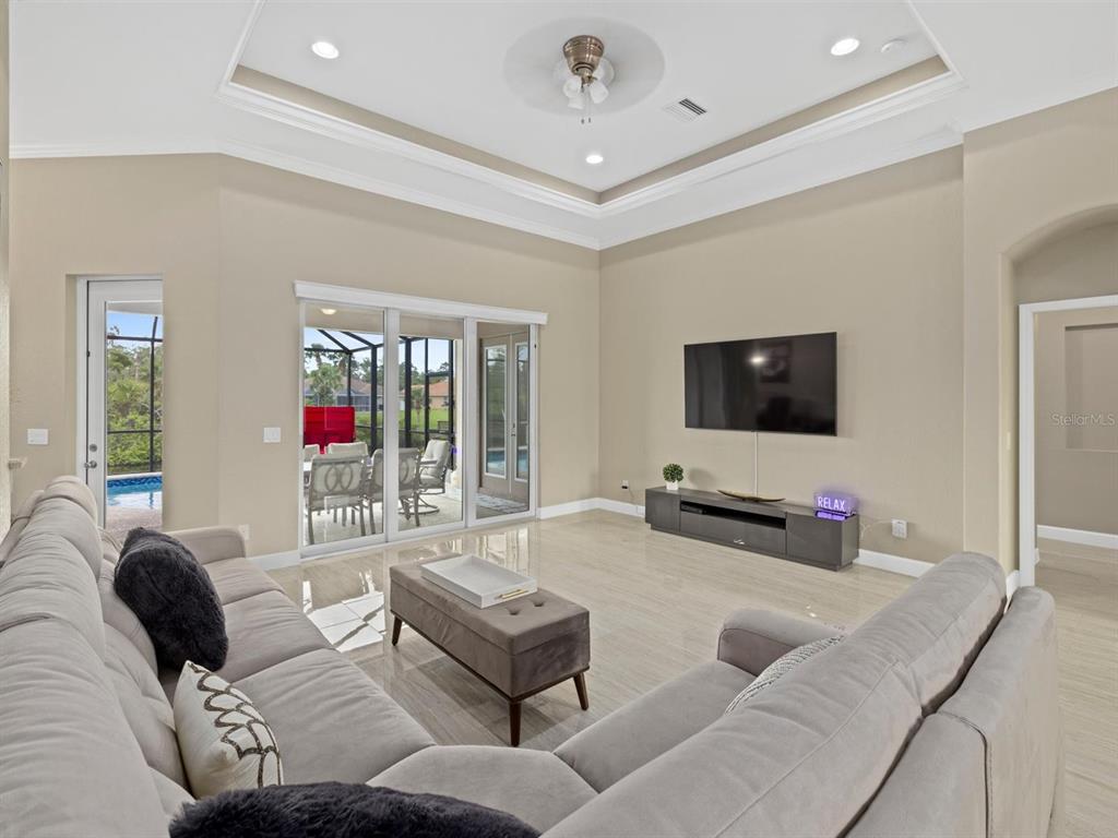 A living room with a tray ceiling, tile floors, a sectional sofa, and sliding glass doors — 340 MCCABE STREET, PORT CHARLOTTE, FL