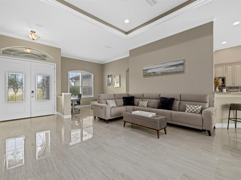 A spacious living room features light tile flooring, a large sectional sofa, and double entry doors — 340 MCCABE STREET, PORT CHARLOTTE, FL