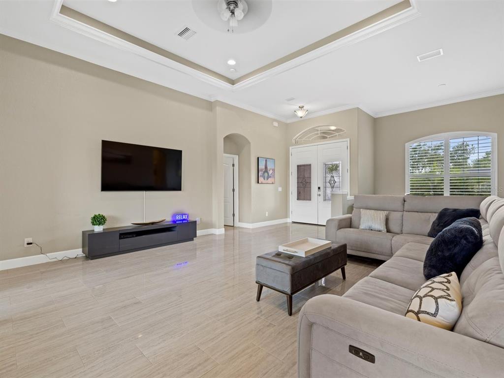 A living room features a wall-mounted television, gray sectional sofa, and light-colored tile flooring — 340 MCCABE STREET, PORT CHARLOTTE, FL