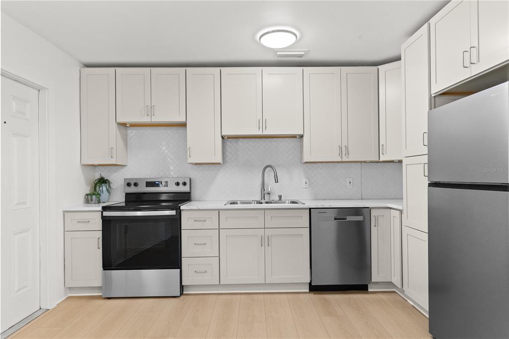 A kitchen with white cabinets, stainless steel appliances, a herringbone backsplash, and light wood flooring — 3663 22ND AVENUE N, ST PETERSBURG, FL