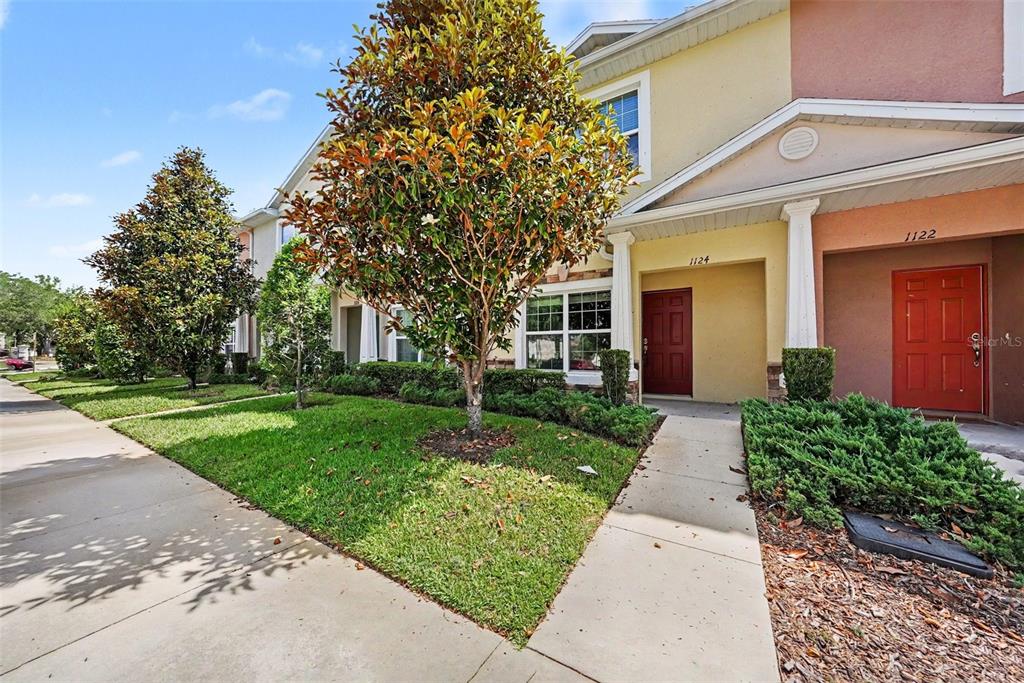 A view of two adjacent townhouses with red front doors and a shared sidewalk — 1124 HILLHURST DRIVE, WESLEY CHAPEL, FL