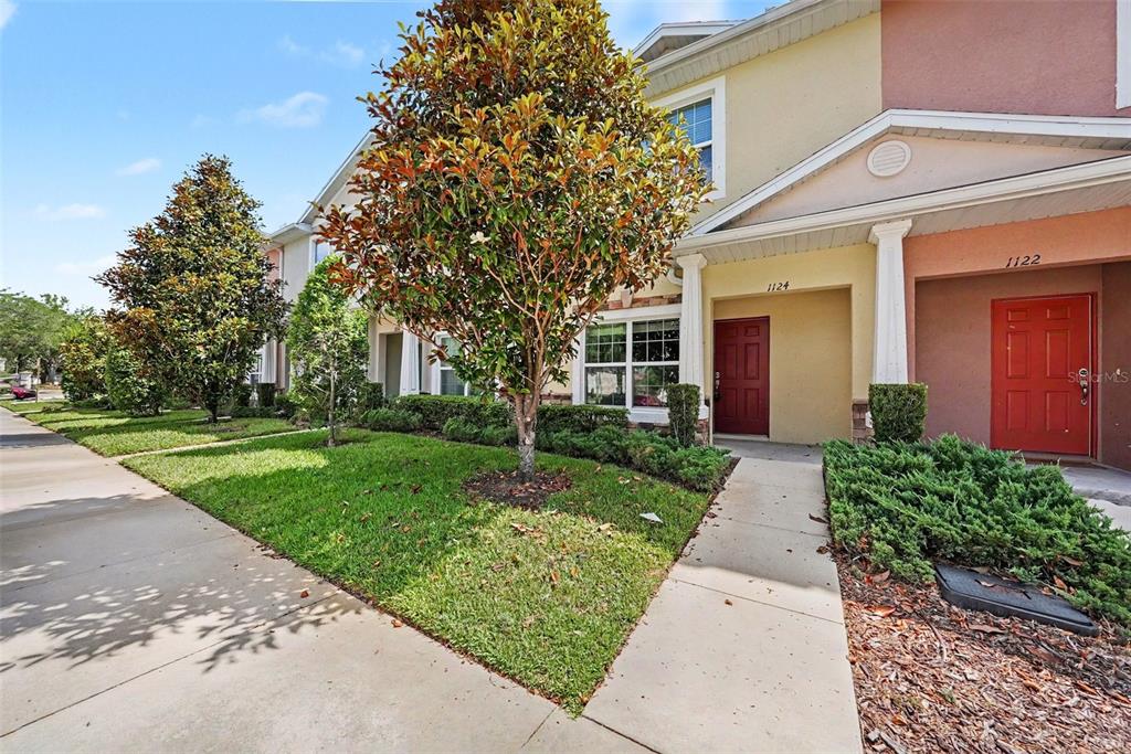 A two-story townhouse exterior features a red front door, a sidewalk, and a front lawn — 1124 HILLHURST DRIVE, WESLEY CHAPEL, FL