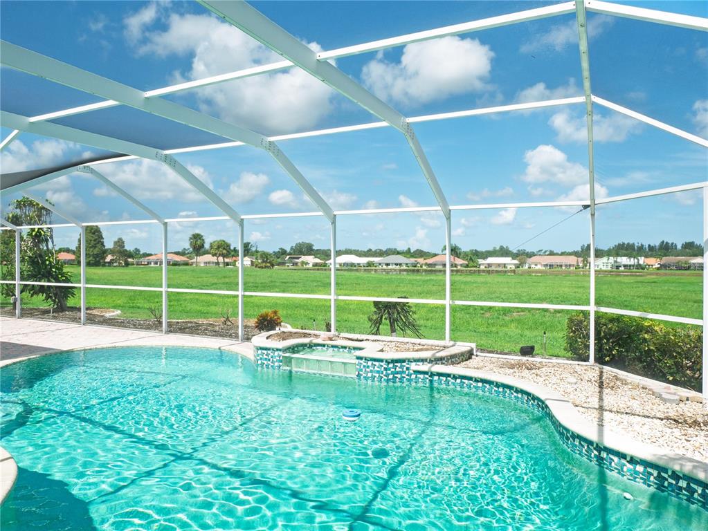 A swimming pool and spa are enclosed by a white screen cage overlooking a grassy field — 1936 WOLF LAUREL DRIVE, SUN CITY CENTER, FL