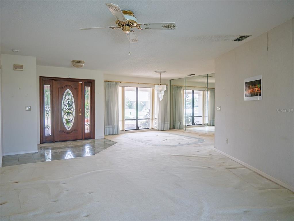 A living room with beige carpeting, a ceiling fan, a chandelier, and a front door — 1936 WOLF LAUREL DRIVE, SUN CITY CENTER, FL