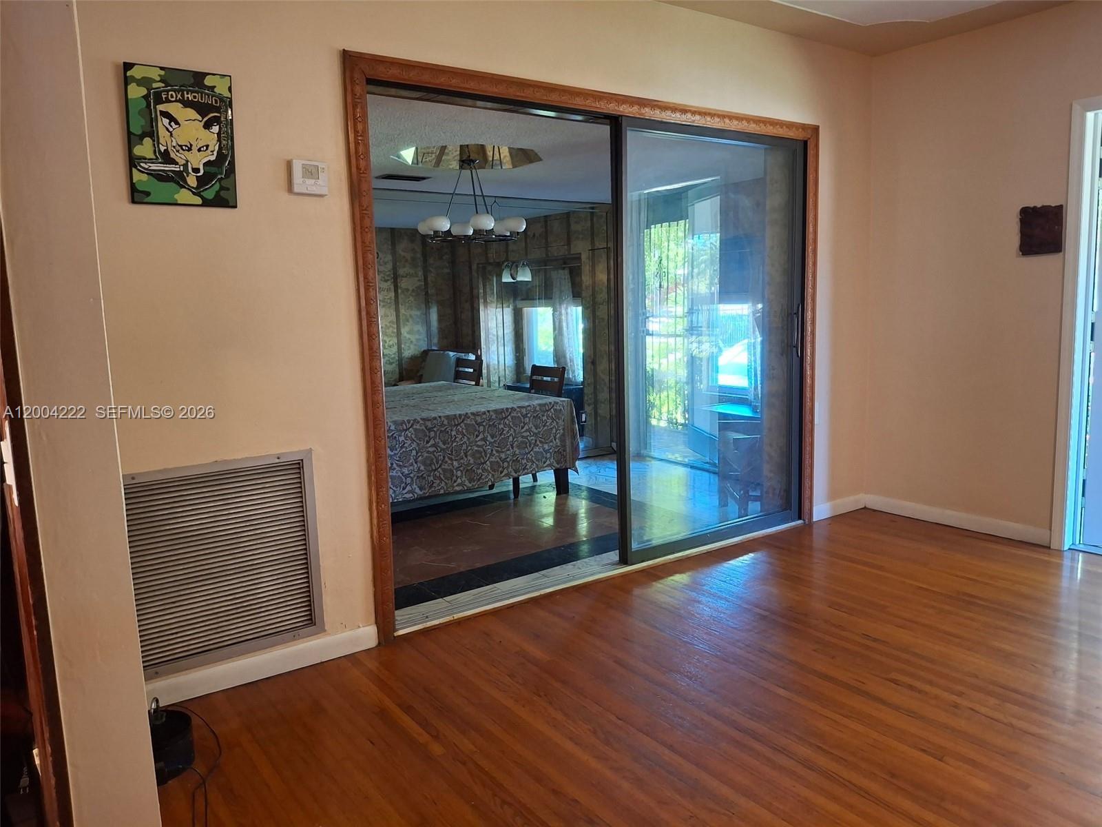 A room with hardwood floors features a large sliding glass door reflecting an adjacent bedroom — 540 SW 39th Ave, Coral Gables FL 33134, CORAL GABLES, FL