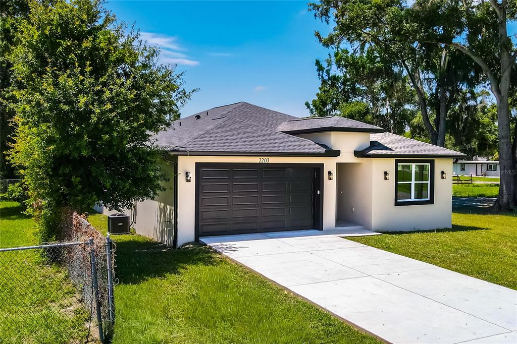 A single-story house with a dark garage door, light exterior walls, and a concrete driveway — 2203 W LOWRY AVENUE, PLANT CITY, FL
