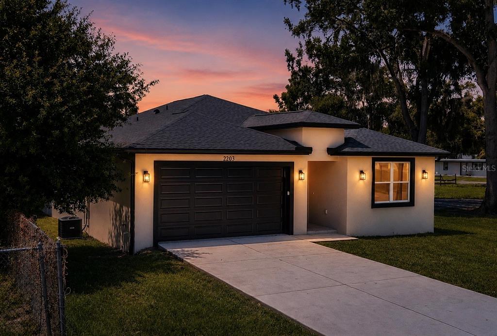 A single-story house with a dark garage door, beige stucco walls, and a concrete driveway — 2203 W LOWRY AVENUE, PLANT CITY, FL