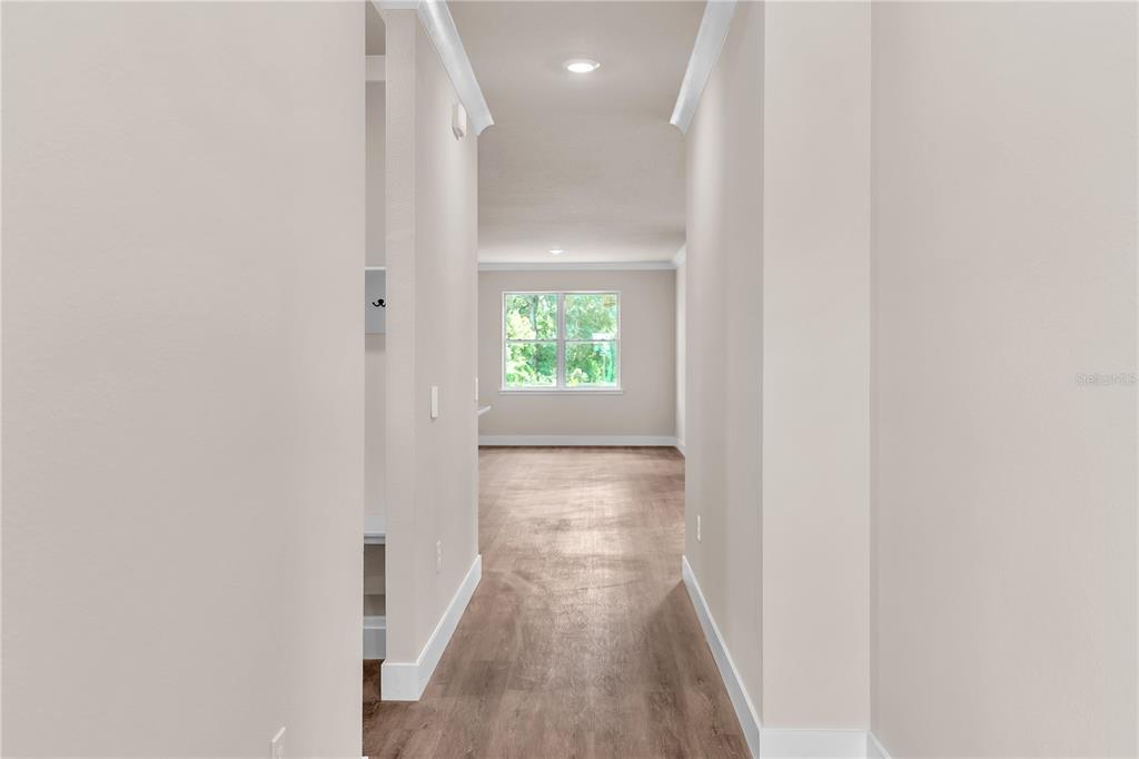 A hallway with light wood-look flooring leads to a room with a large window — 2203 W LOWRY AVENUE, PLANT CITY, FL