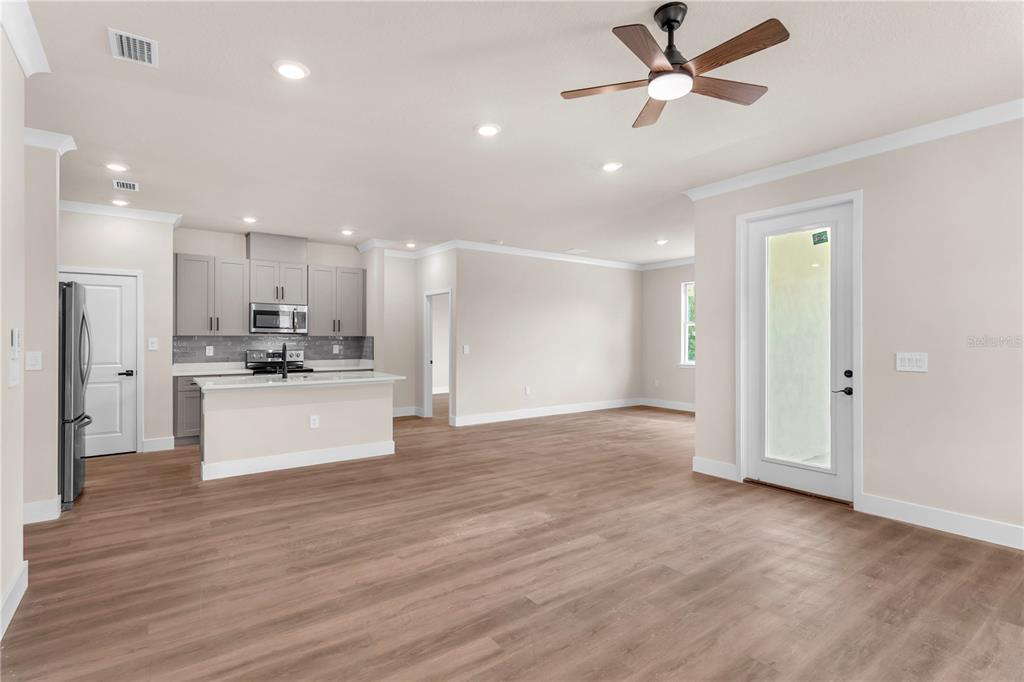 An open-concept living area features light wood-look flooring, gray kitchen cabinets, and a ceiling fan — 2203 W LOWRY AVENUE, PLANT CITY, FL