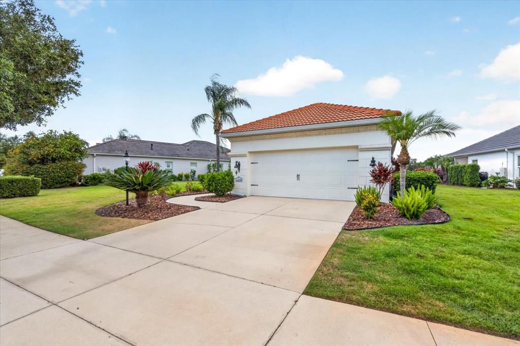 A white house with a two-car garage and a tiled roof sits on a lawn — 12186 WAKULLA PLACE, VENICE, FL