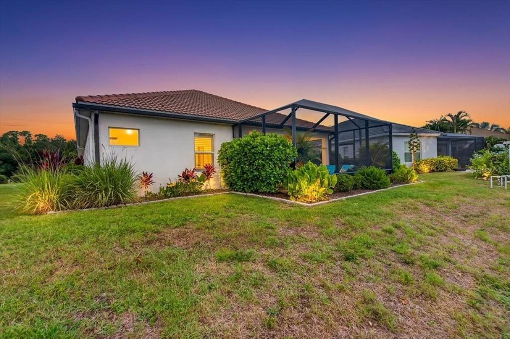 A single-story house with a screened-in lanai sits on a grassy lawn at sunset — 12186 WAKULLA PLACE, VENICE, FL