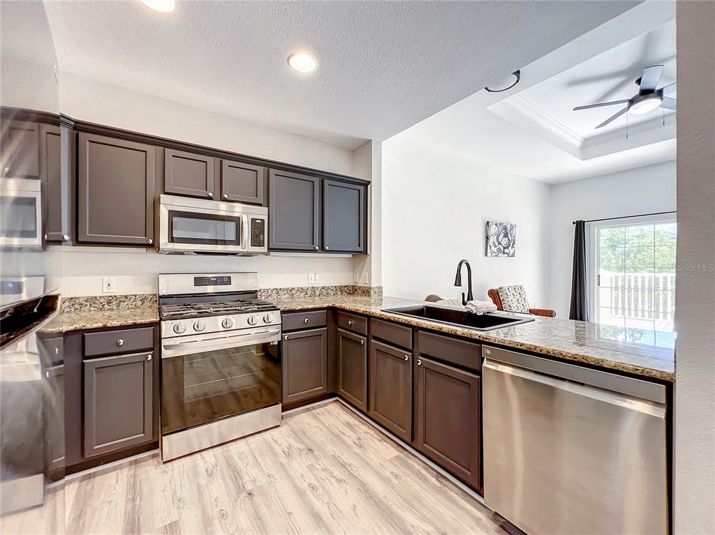 A kitchen features dark brown cabinets, granite countertops, stainless steel appliances, and light wood flooring — 7510 SEVEN EAGLES WAY, REUNION, FL