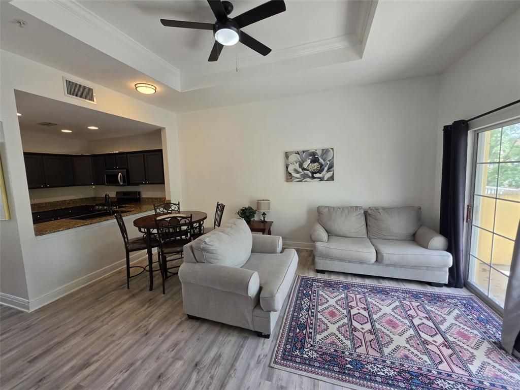A living room with light wood floors, a dining area, and a kitchen with dark cabinets — 7510 SEVEN EAGLES WAY, REUNION, FL