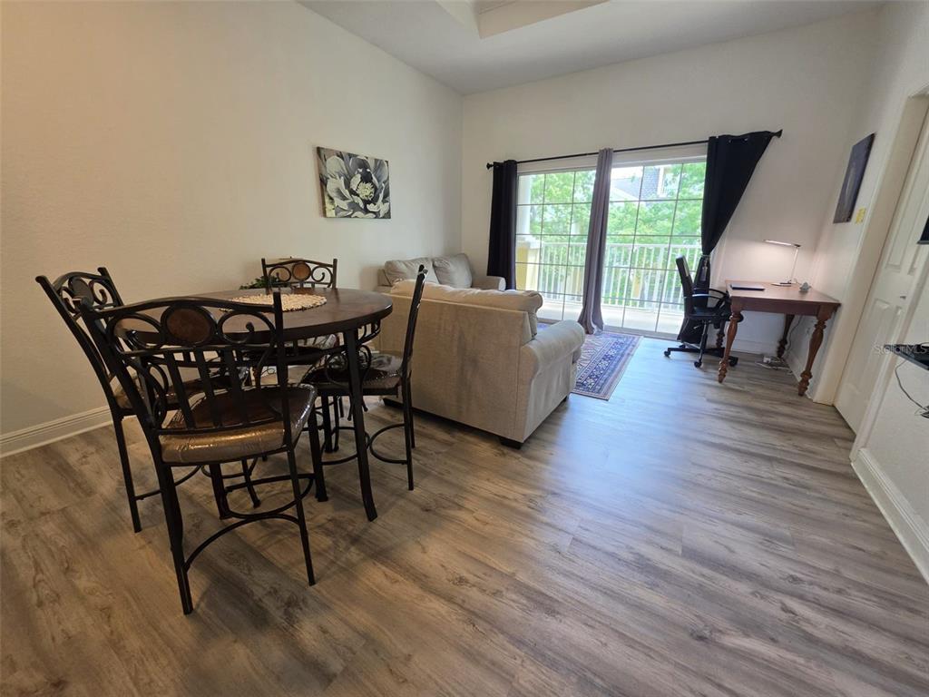 A living and dining area features wood-look flooring, a balcony, and a desk space — 7510 SEVEN EAGLES WAY, REUNION, FL