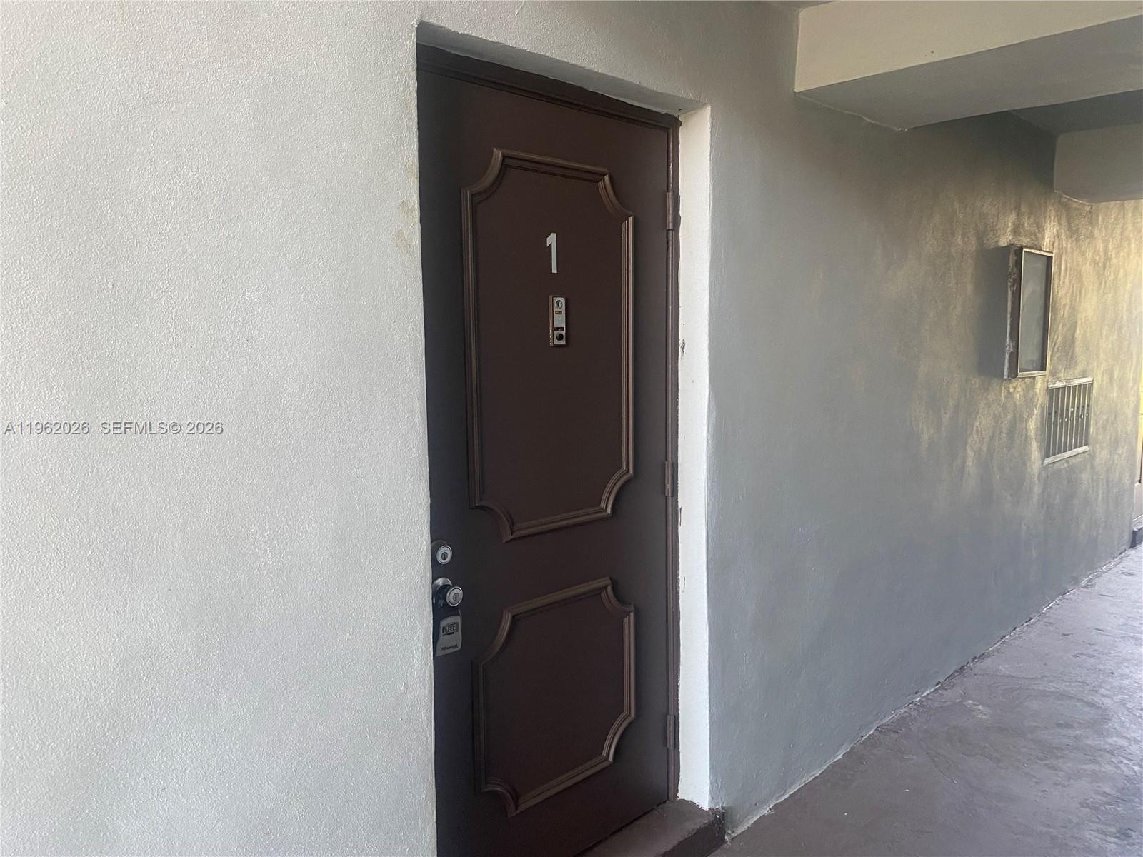 A brown door marked with the number one is set into a plain gray wall — 335 W Laurel Dr # 1M, Margate FL 33063, MARGATE, FL