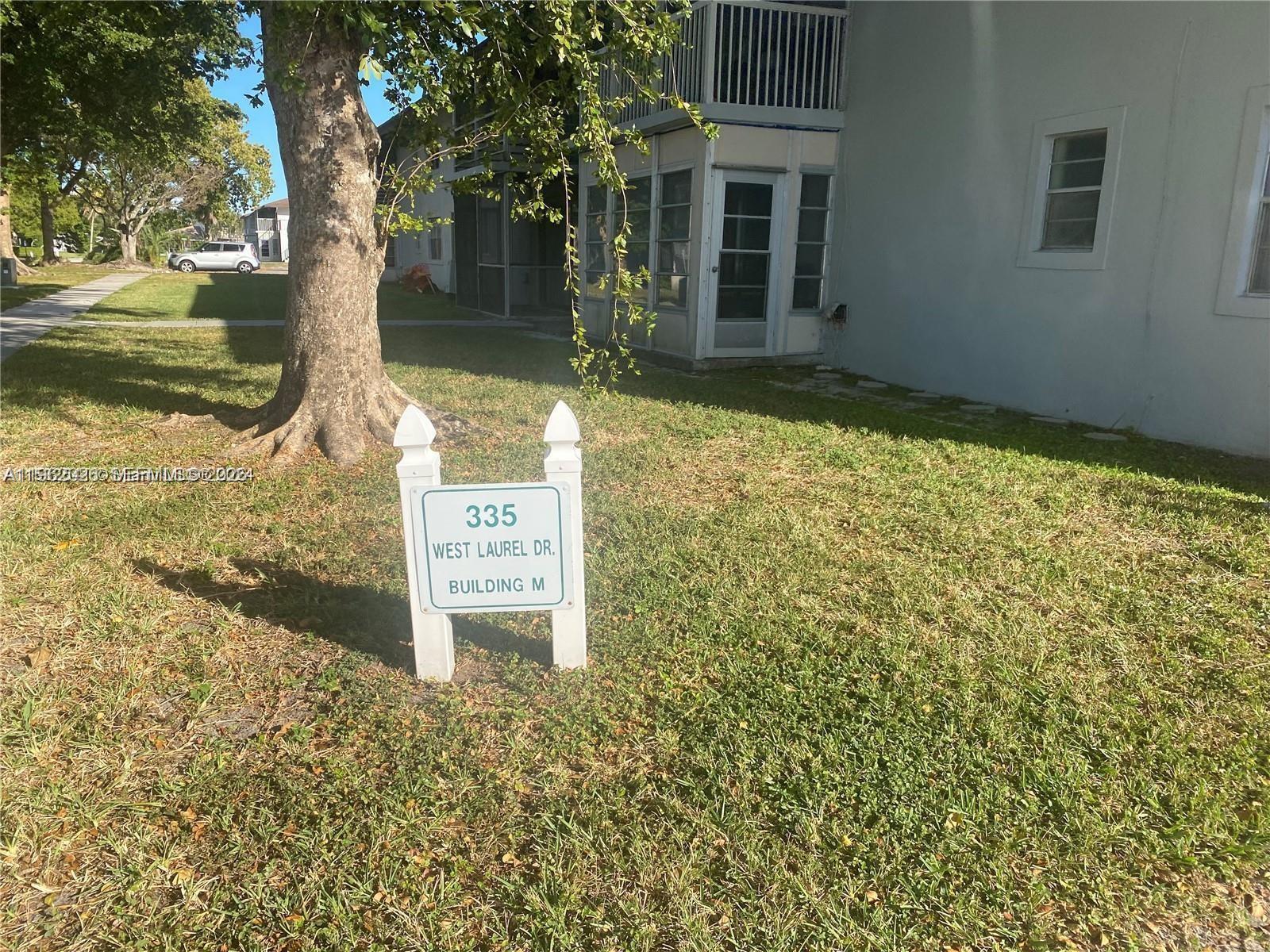 A white sign stands in a grassy yard in front of a multi-story building — 335 W Laurel Dr # 1M, Margate FL 33063, MARGATE, FL