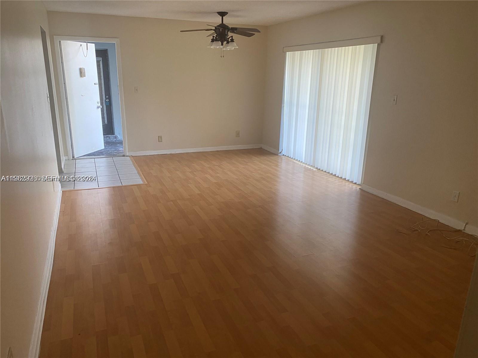 An empty living room features light wood-look flooring, a ceiling fan, and vertical window blinds — 335 W Laurel Dr # 1M, Margate FL 33063, MARGATE, FL