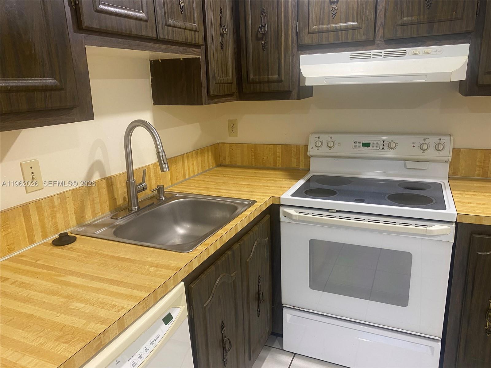 A kitchen features dark wood cabinets, a stainless steel sink, and a white electric stove — 335 W Laurel Dr # 1M, Margate FL 33063, MARGATE, FL