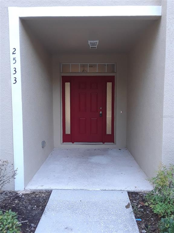 A recessed entryway features a red front door with sidelights and a concrete porch — 2533 OLD KENT CIRCLE, KISSIMMEE, FL