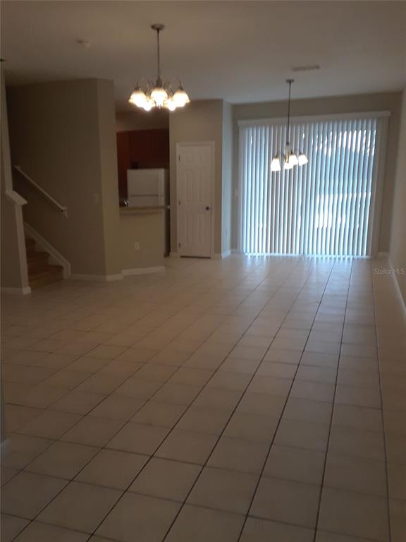 An open-concept living and dining area features tile flooring, two chandeliers, and a sliding door — 2533 OLD KENT CIRCLE, KISSIMMEE, FL