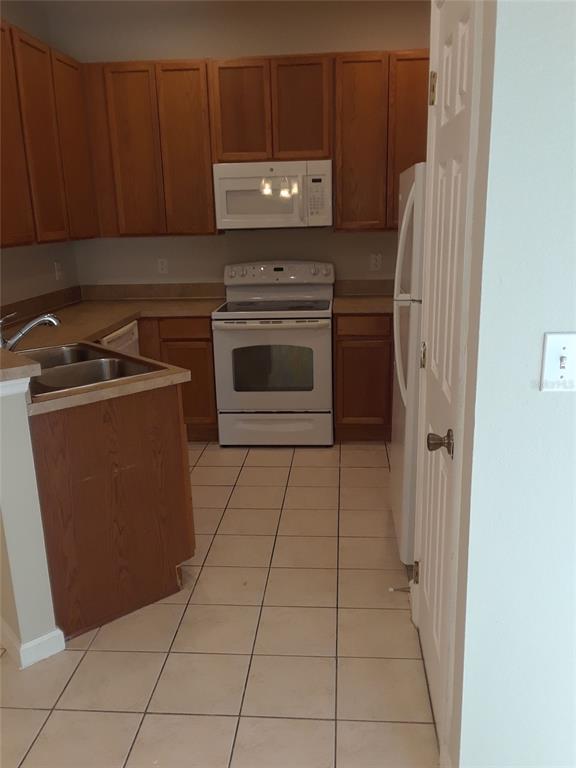A kitchen features wood cabinets, white appliances, a double sink, and light-colored tile flooring — 2533 OLD KENT CIRCLE, KISSIMMEE, FL