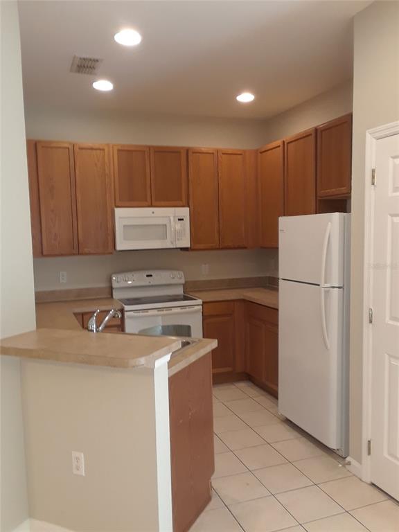 A kitchen features wood cabinets, white appliances, a tiled floor, and a breakfast bar — 2533 OLD KENT CIRCLE, KISSIMMEE, FL