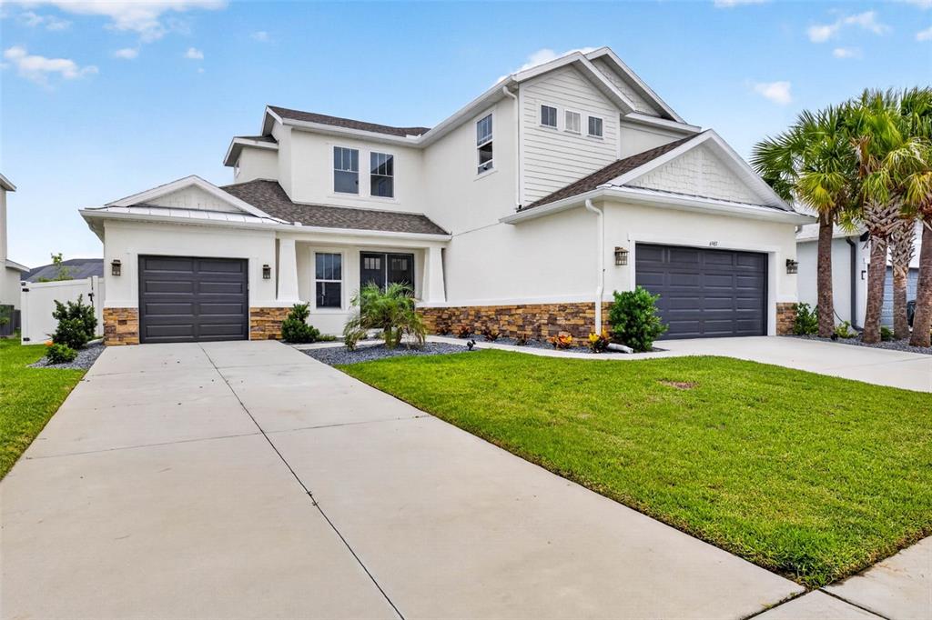 A two-story house with a white exterior, stone veneer base, and two dark garage doors — 6967 TALAMORE DR, WESLEY CHAPEL, FL
