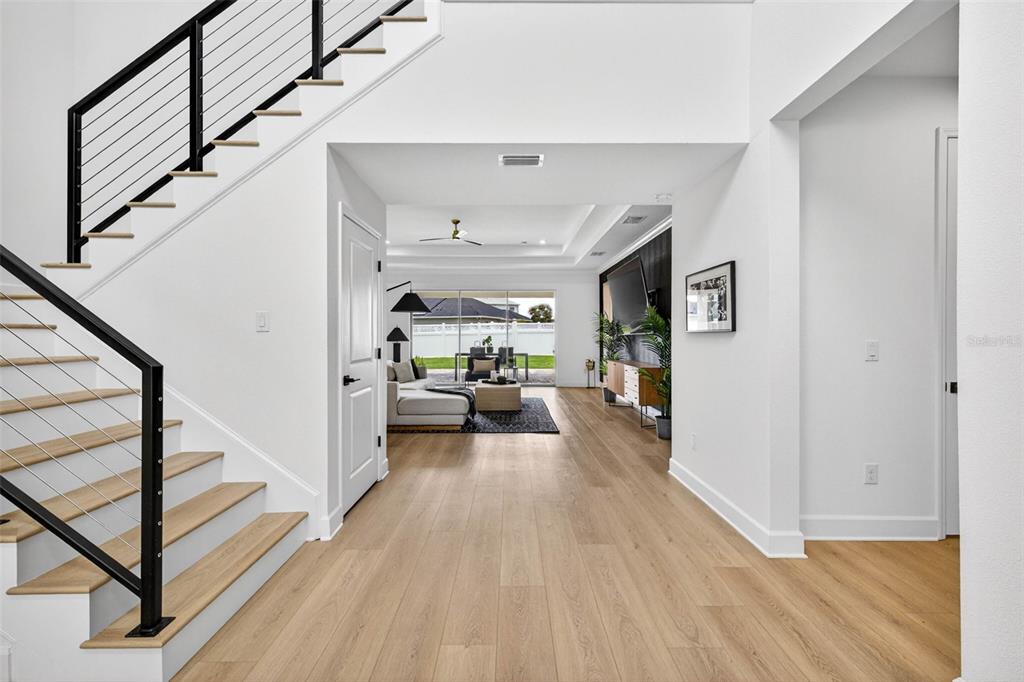 A bright entryway with light wood flooring leads to an open living area with stairs — 6967 TALAMORE DR, WESLEY CHAPEL, FL
