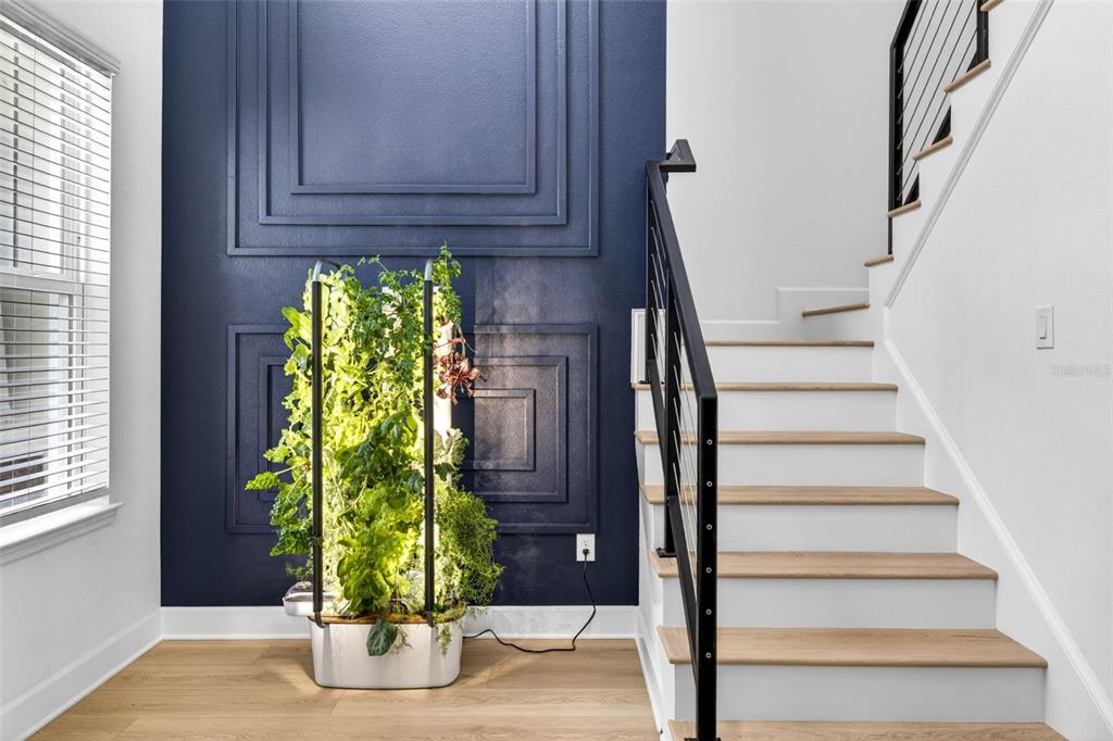 A vertical hydroponic garden stands next to a staircase with wood treads and black railings — 6967 TALAMORE DR, WESLEY CHAPEL, FL