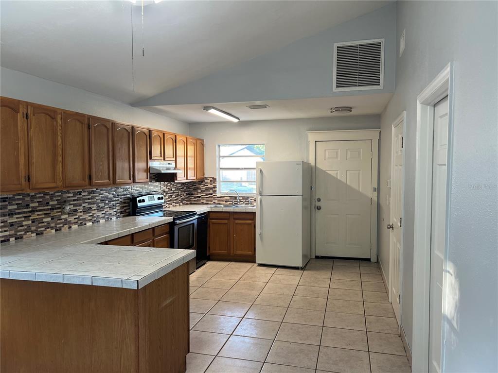 A kitchen features wood cabinets, tile countertops, a tiled backsplash, and white appliances — 4843 BILLY DIRECT LANE, LUTZ, FL
