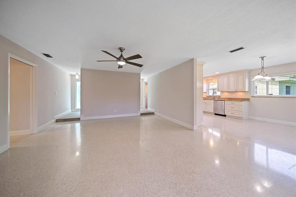 A spacious living room with polished terrazzo floors leads into a bright, white-cabinet kitchen — 1163 60TH AVENUE S, ST PETERSBURG, FL