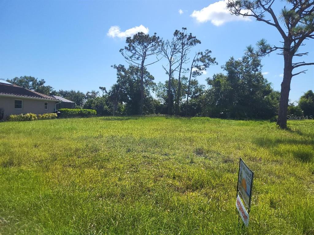 A grassy vacant lot with a for sale sign and trees in the background — 20 PINEHURST PLACE, ROTONDA WEST, FL