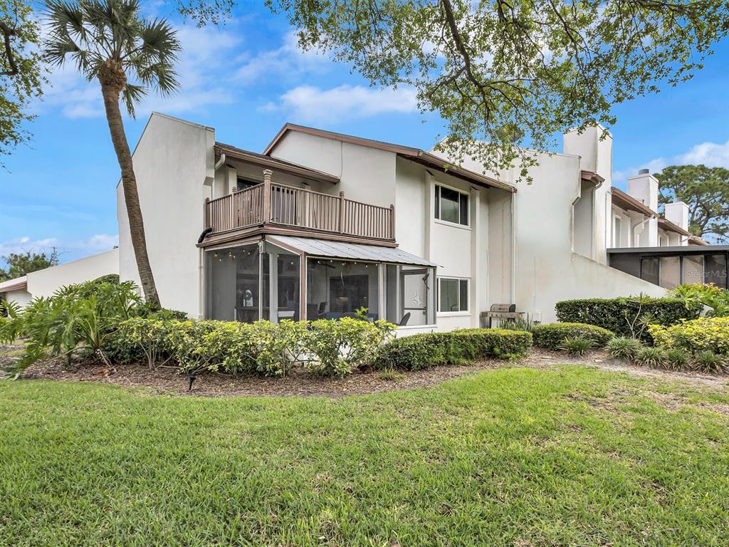 A two-story townhouse exterior features a screened-in patio, a wooden balcony, and surrounding landscaping — 7581 CUMBERLAND ROAD UNIT 7, SEMINOLE, FL