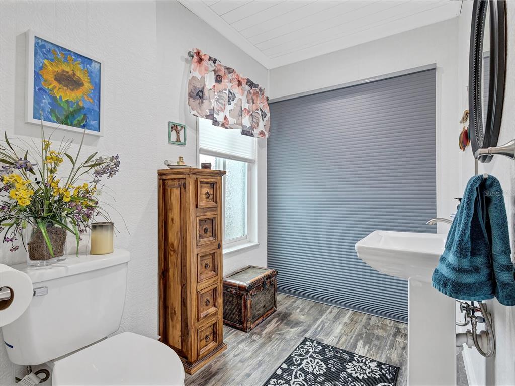 A bathroom features a pedestal sink, a toilet, a wooden storage cabinet, and wood-look flooring — 7581 CUMBERLAND ROAD UNIT 7, SEMINOLE, FL