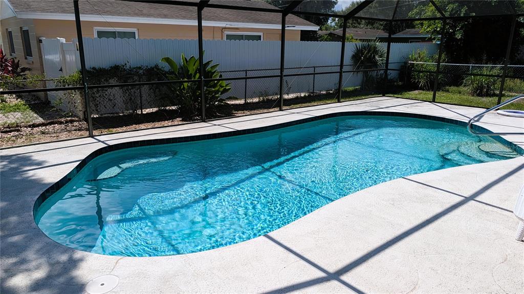 A swimming pool with a screen enclosure sits in a backyard with a white fence — 5350 CASTLEMAN DRIVE, SARASOTA, FL