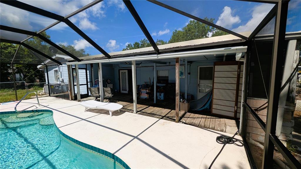 A swimming pool sits beside a covered wooden deck attached to a blue house — 5350 CASTLEMAN DRIVE, SARASOTA, FL