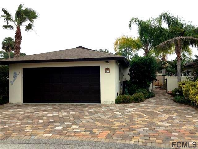 A single-story house with a dark garage door and a paved driveway surrounded by palm trees — 87 CLUB HOUSE DRIVE, PALM COAST, FL