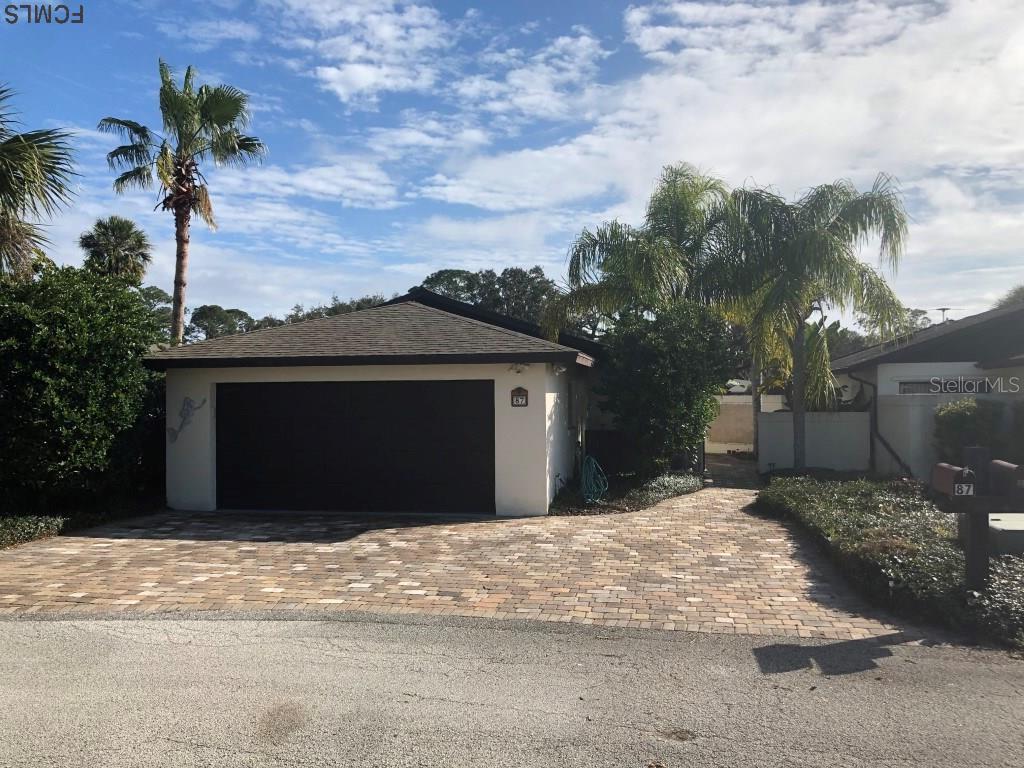 A single-story house with a dark garage door and a paved driveway under a blue sky — 87 CLUB HOUSE DRIVE, PALM COAST, FL