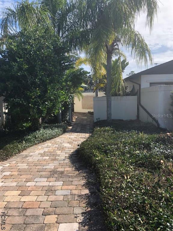A paved walkway leads toward a house entrance framed by a palm tree and landscaping — 87 CLUB HOUSE DRIVE, PALM COAST, FL