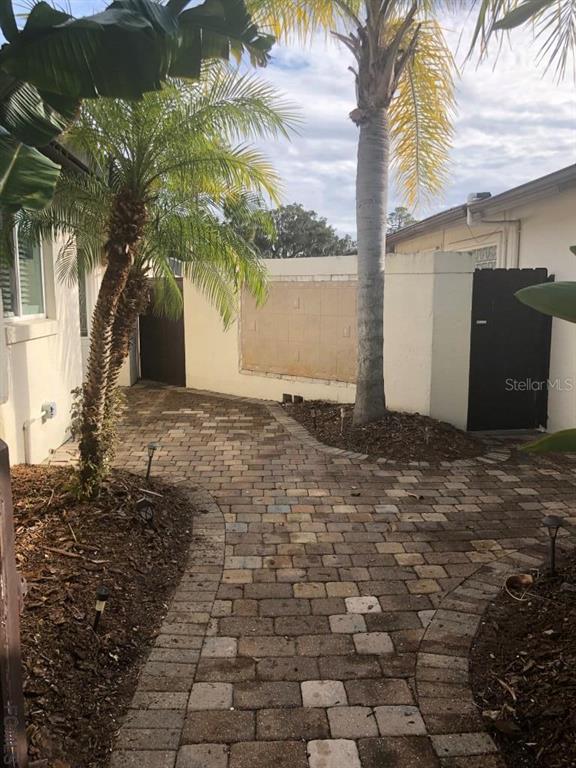 A paved walkway leads through a courtyard featuring palm trees and a stucco wall — 87 CLUB HOUSE DRIVE, PALM COAST, FL