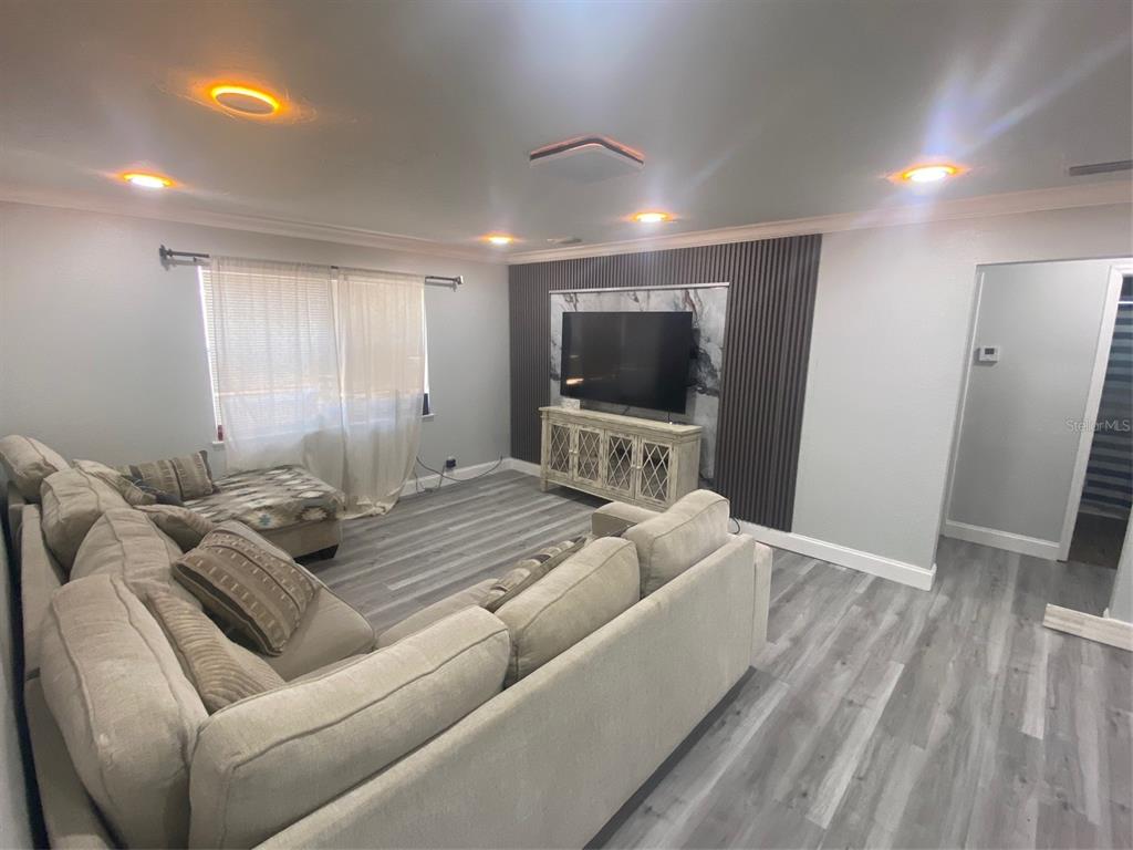 A living room features gray wood-look flooring, a sectional sofa, and a slatted accent wall — 3303 19TH STREET COURT E, BRADENTON, FL