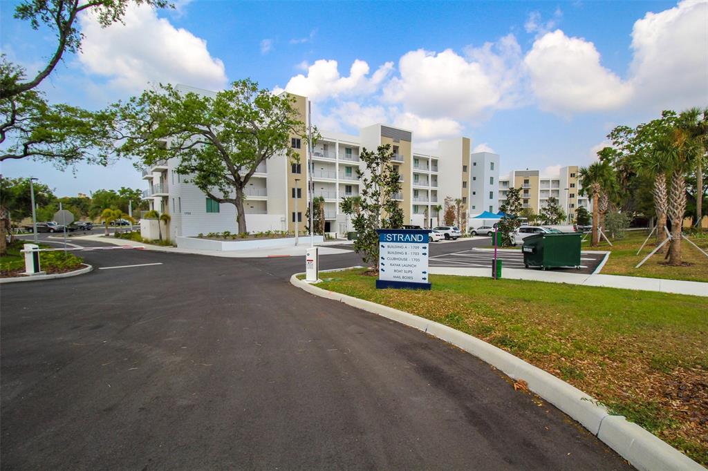 An exterior view of a modern apartment complex with a directional sign and parking lot — 1703 N TAMIAMI TRAIL UNIT B406, SARASOTA, FL